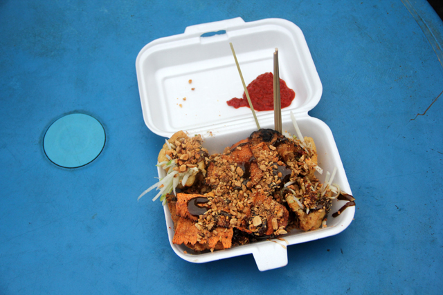 Smoky satay grills and crowded tables lining Jalan Alor food street at night in Kuala Lumpur