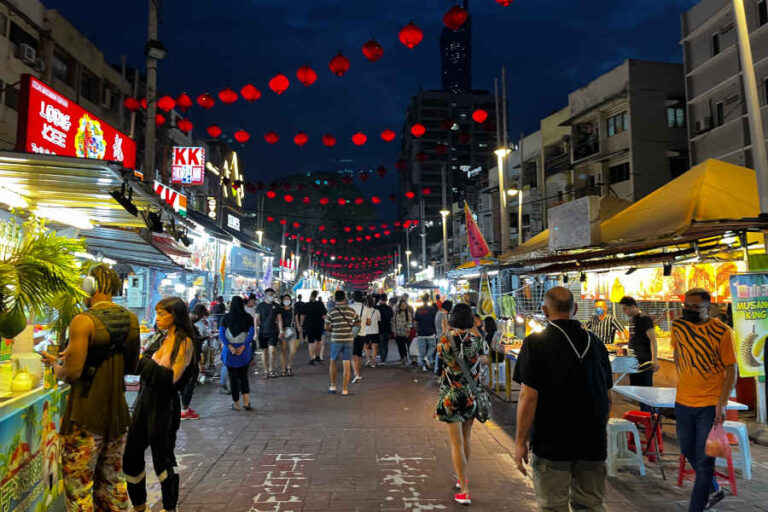 Rows of open-air hawker tables and neon signs along Jalan Alor food street at night